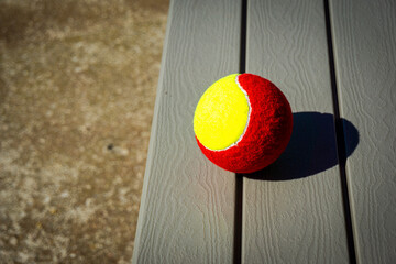 One red and yellow tennis ball on a wooden bench. Summer activity