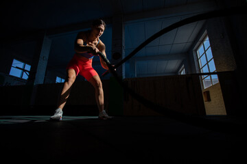 Fototapeta na wymiar Athletic woman doing double wave exercise with ropes in crossfit gym.
