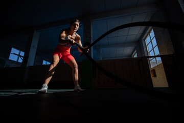 Athletic woman doing double wave exercise with ropes in crossfit gym.