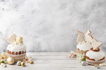 Set of traditional easter cakes with icing, decorated with gingerbread cookies in shape of rabbits and birds over white wooden background. Side view, copy space. Easter treat, holiday symbol