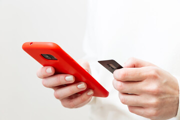 Close up of female hands holding credit card and using smartphone in red case on white background. Woman paying securely online, using banking service, ordering in internet store. Online shopping.