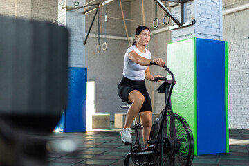 Athletic woman training on assault bike in crossfit gym.