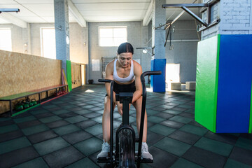 Fototapeta na wymiar Athletic woman training on assault bike in crossfit gym.
