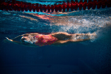 Muscular athlete. Competitive woman, professional female swimmer training in swimming pool indoor. Underwater view. Concept of sport, endurance, competition, energy, healthy lifestyle