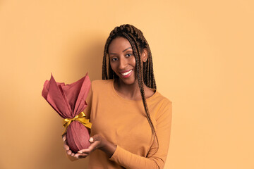 happy black young woman celebrating easter egg gift in beige studio background. holiday, easter,...