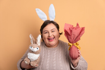 happy plus size woman with easter bunny in beige background. holiday, easter, celebration concept.
