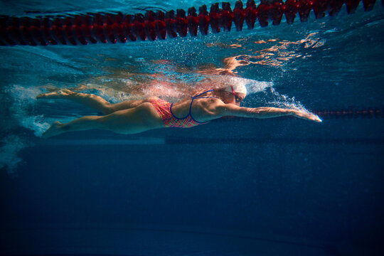 Side view dynamic image. Professional female swimmer training in swimming pool indoor. Underwater view. Concept of sport, endurance, competition, energy, healthy lifestyle