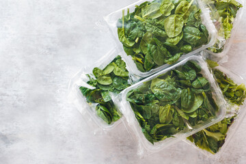 Spinach and Japanese mizuna packaged in clear plastic containers on rustic background. Top view, blank space

