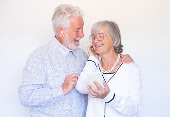 Cheerful senior couple having fun listening music with same earphones, smiling man and woman holding smart phone enjoying relax together