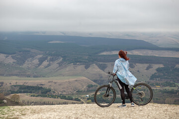 A woman at the top of a mountain with a bicycle looks at the admiring mountain panorama during a...