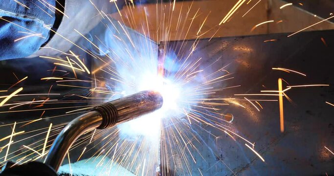 A worker use a welding machine to weld a piece of metal. Sparks and flame in metalworking. 4k video.