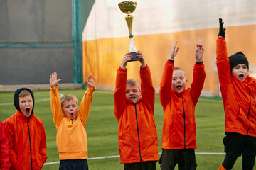 Winners. Group of little boys, children in uniform, football players raising award, trophy. Kids...