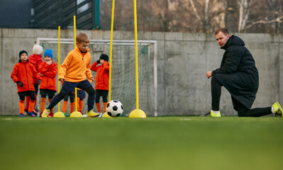 Doing dribbling exercises. Football coach training, teaching kids, boys to play. Outdoor game on sports field. Concept of sport, childhood, active lifestyle, hobby, sport club