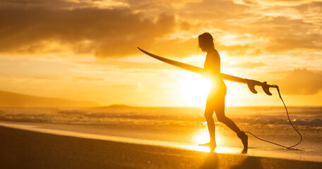 A silhouette of a girl surfer on the beach at sunset. A woman walking from the ocean after surf on...