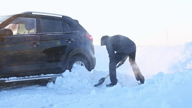 A man with a shovel digs out a car stuck in the snow