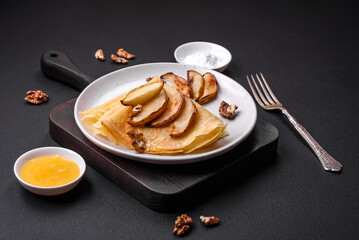 Delicious fresh baked pancakes with honey and fruits on a concrete background