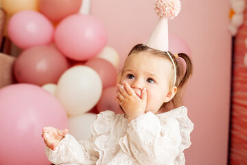 Cute baby eating cake for first birthday. Baby girl in dress. Festive decor in pink colors