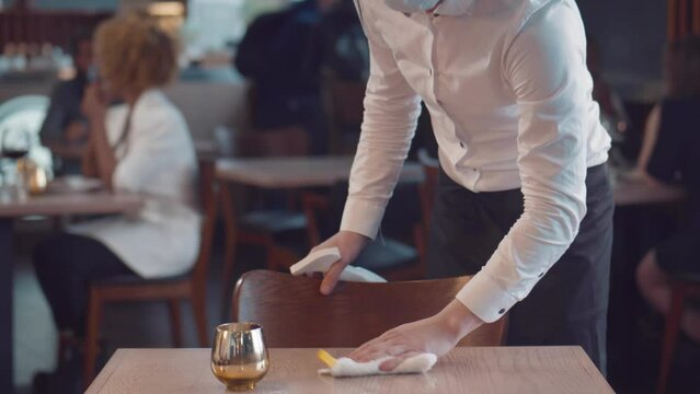 Young waiter wearing mask and cleaning table in cafe. Realtime
