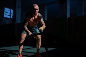 Fototapeta na wymiar Athletic man doing double wave exercise with ropes in crossfit gym.