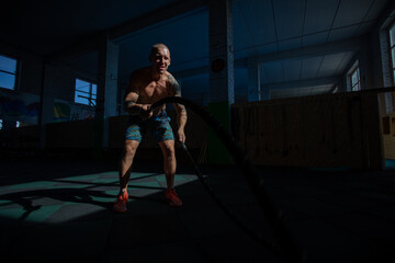 Athletic man doing double wave exercise with ropes in crossfit gym.