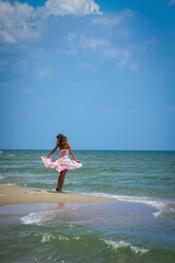 Fototapeta premium Young beautiful slim woman wearing in a dress dancing on the seashore in the sunrays. Holiday, sommer travel, rest concept. Vertical image.