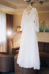 Fototapeta na wymiar The perfect wedding dress with a full skirt on a hanger in the room of the bride with blue curtains