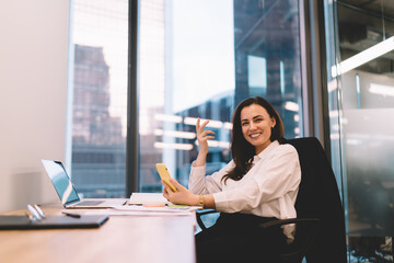 Smiling woman sitting at table with laptop and smartphone in office