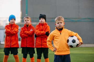 Group of boys, children, football players in uniform standing in a line on sports field grass...
