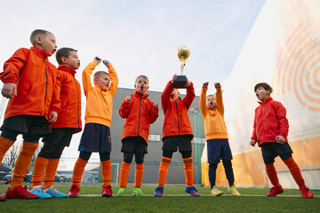 Happiness. Group of little boys, children in uniform, football players raising award, trophy. Kids...