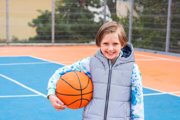 a sports boy in a sweater and vest stands on the basketball court, holds the ball in his hands,...
