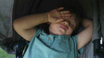One tired small boy awake after nap sitting inside stroller. Exhausted child not wanting to get up....