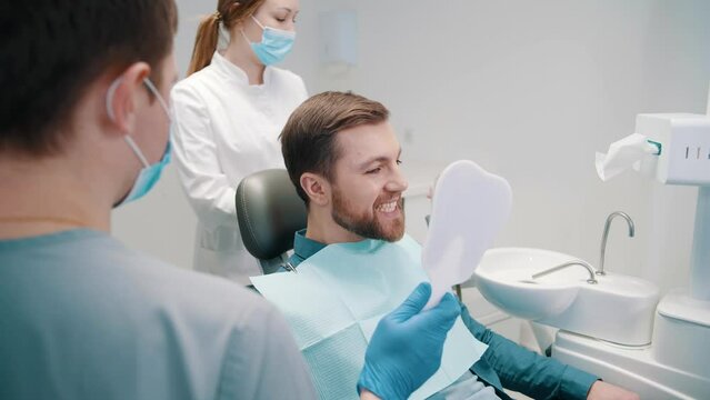 Professional male dentist show beautiful teeth in mirror to man visitor
