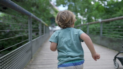 One active small boy running outdoors at park crossing bridge. Back of child runner in slow motion...