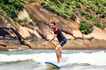 mid adult caucasian man riding a small wave learning to surf in Brazil