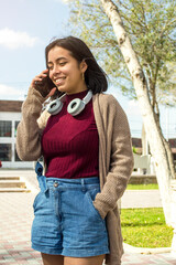 Joven chica con auriculares respondiendo llamada telefónica en una plaza al aire libre.