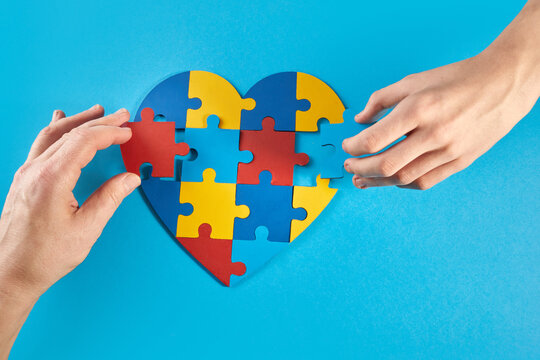 Father and autistic son hands holding jigsaw puzzle heart shape. World Autism Awareness Day