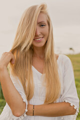 Close up portrait of blond charming woman with wonderful smile and long hair posing to camera outside on sunlight 