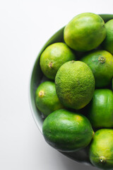 Top view of green limes in a bowl with white background