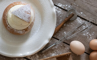 Homemade semla dusted with icing sugar on a blue plate in a country kitchen