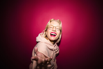 A playful young blond woman is posing isolated on magenta background while laughing at the camera. Viva magenta.