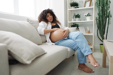 Pregnant woman headache lies at home in a shirt and jeans on the couch fatigue and heaviness in the last month of pregnancy before childbirth, motherhood difficulties, nausea