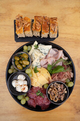 Antipasto. Top view of a dish with sliced salami, cheese, blue cheese, focaccia bread, italian boconccinos, walnuts, ham, cured ham and green olives on the wooden table.