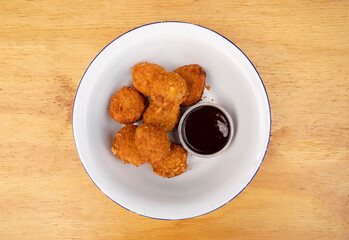 Top view of fried chicken balls with a spicy sauce in a white bowl on the wooden table.