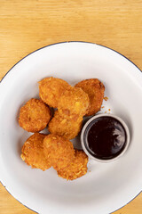 Closeup view of fried chicken balls with a spicy sauce in a white bowl.