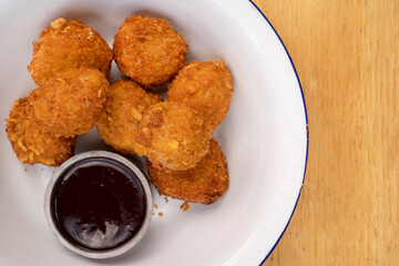 Top view of fried chicken balls with a spicy sauce in a white bowl on the wooden table. 