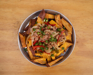 Top view of a metal dish with sweet potato fries with a spicy sauce made with peppers, cheddar cheese, onion and pork sausages.