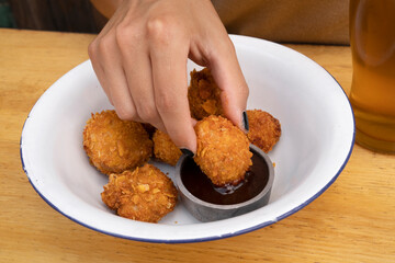 Closeup view of a female hand dipping a fried chicken croquette in spicy sauce. 