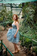 portrait of beautiful smiling romantic redhead woman in blue dress walking desert botanical garden with cactuses