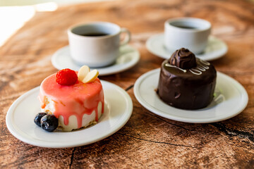 Colorful small fruity cupcakes on small white plates and cups of black coffee on wooden structure background