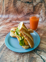 Baguette with lettuce and chicken cutted half with glass of carrot juice